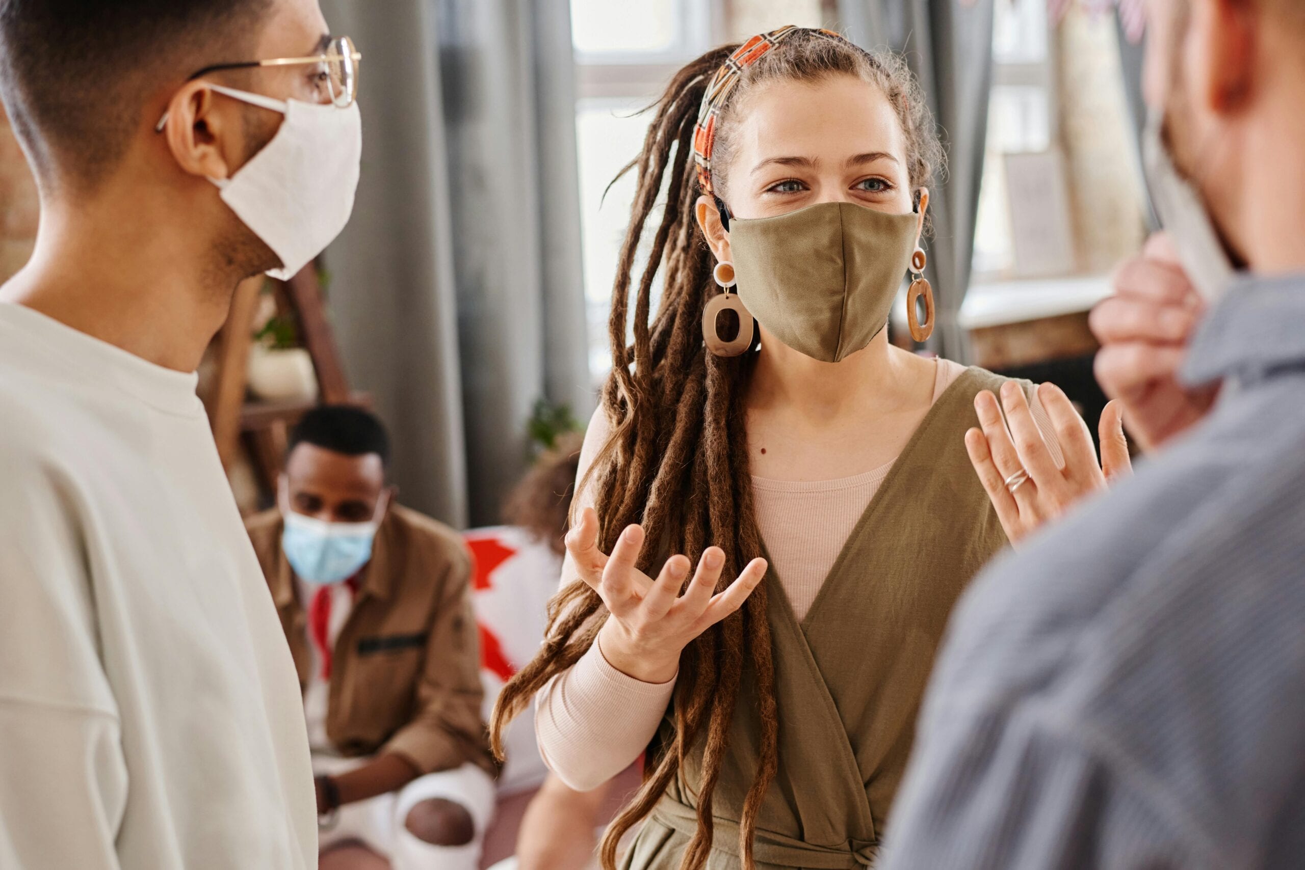 A group of diverse adults communicating indoors while wearing face masks.
