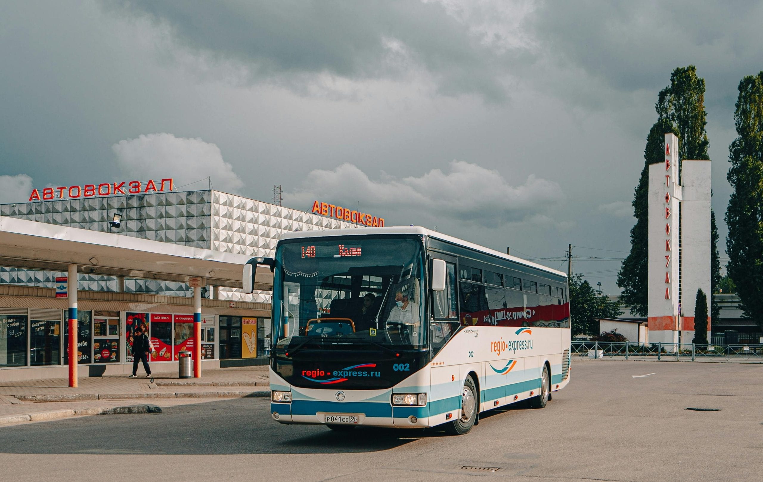 City bus station featuring modern architecture and a parked bus under cloudy skies.