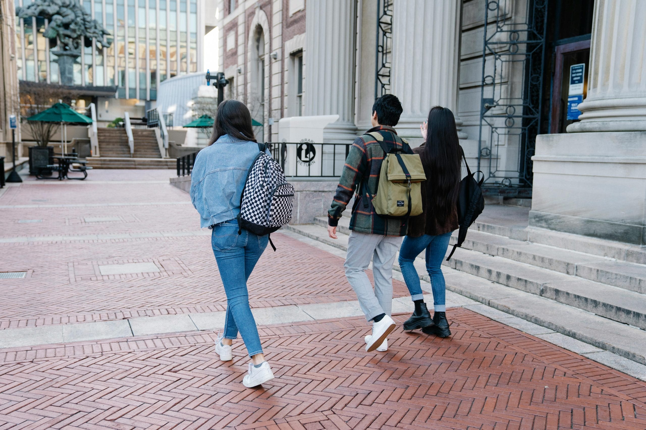 A group of young students walk along a university campus pathway, carrying backpacks.