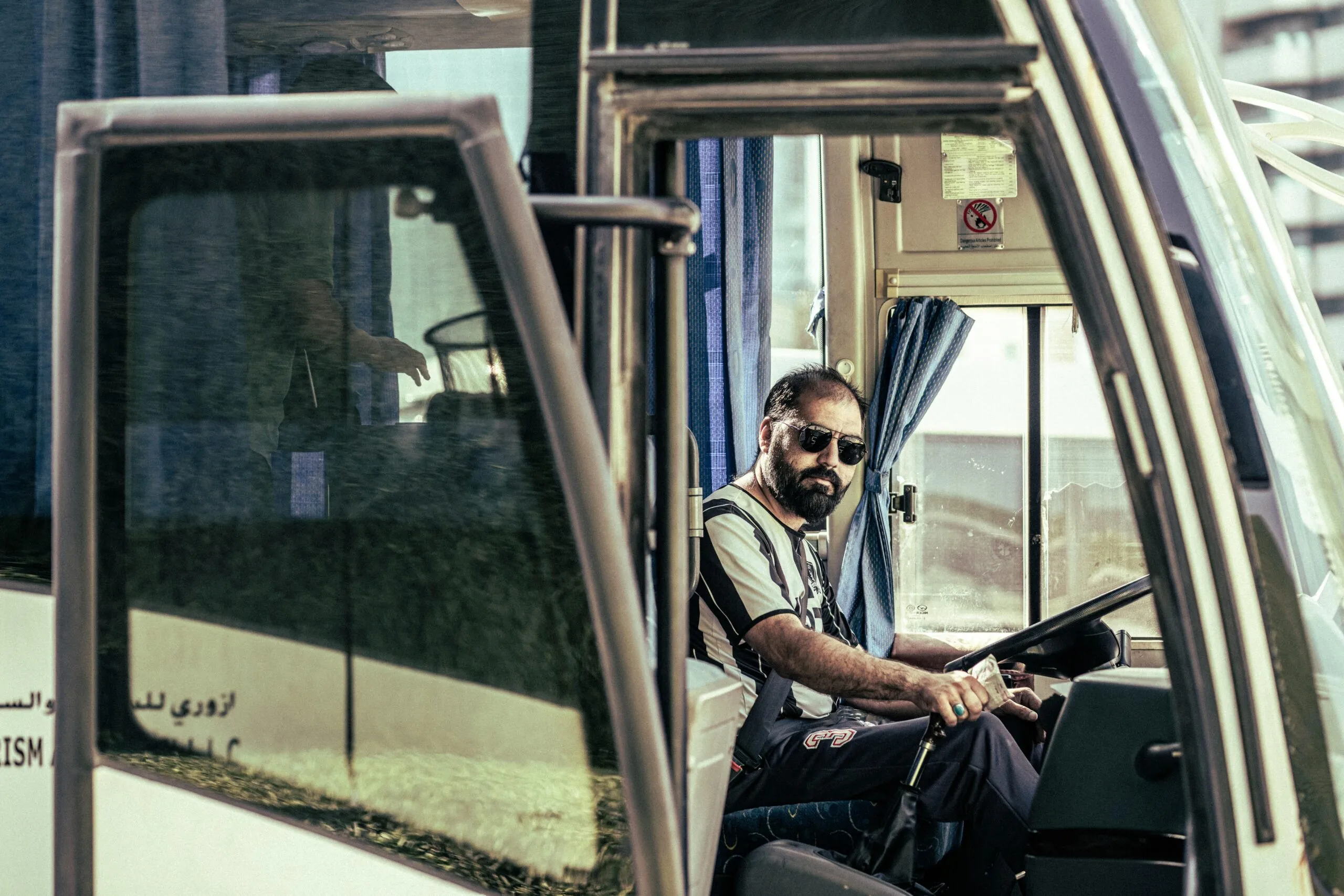Confident bus driver in sunglasses sits behind the wheel, ready for travel.