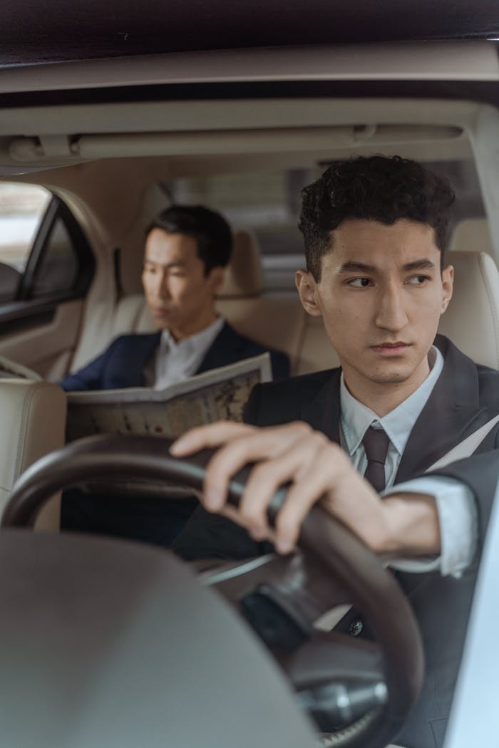 Chauffer Driving a Car and a Passenger Reading a Newspaper in the Backseat